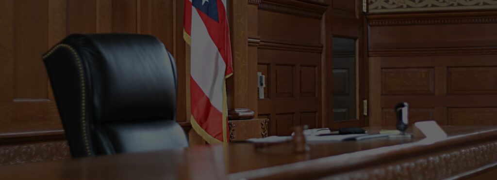 A judge’s empty chair and desk with a gavel, plus a U.S. flag in the background, evoke the solemnity of justice.